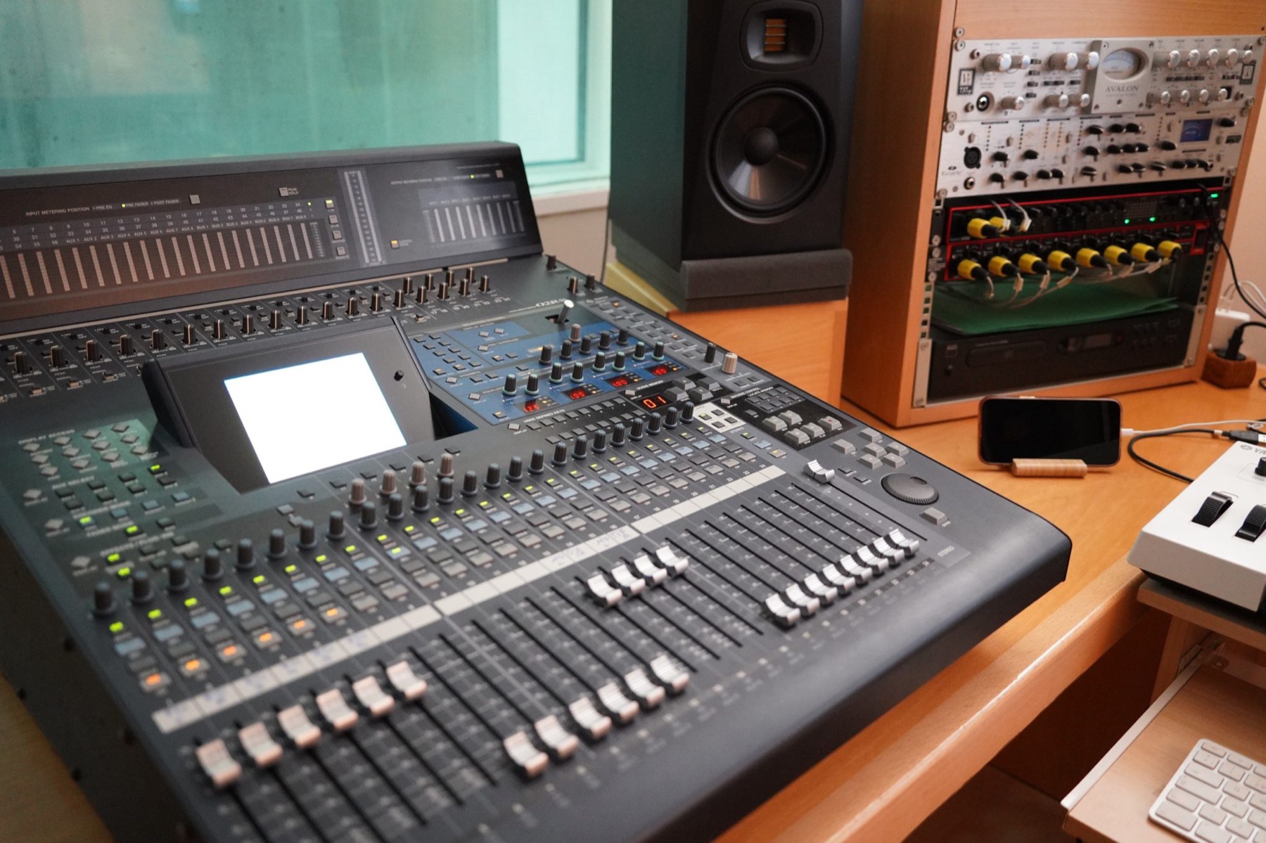 A digital mixing console beside studio monitors and an outboard equipment rack
